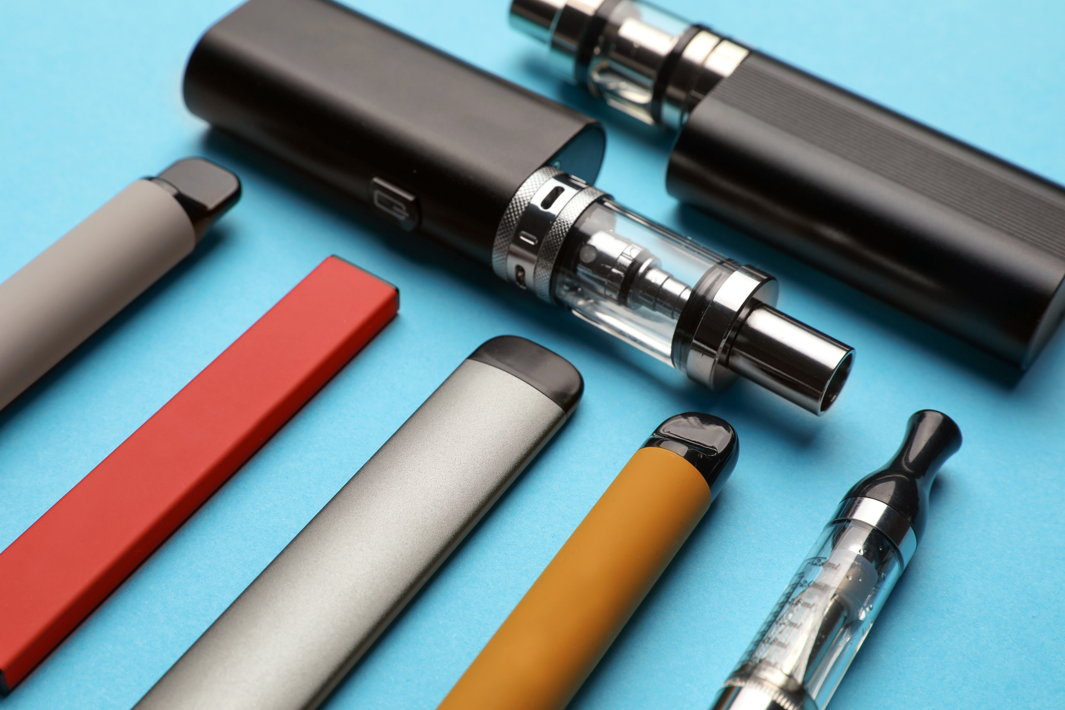 Différentes cigarettes électroniques sur un fond bleu pâle, gros plan.
